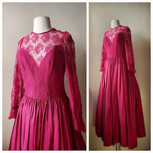 May include: A magenta-colored vintage dress with a high neckline and long sleeves. The bodice features a V-neck design with intricate lace detailing. The long sleeves are made of lace, and the skirt is a full, flowing style.