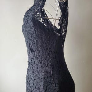 May include: A black lace dress with a halter neckline. The dress is displayed on a white wire dress form. The dress has a fitted silhouette and a floral lace pattern. The dress is a formal wear item.