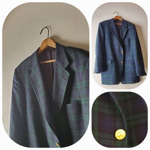 Può includere: Un blazer a quadri blu navy e verde con bottoni dorati, appeso a una gruccia di legno. Il blazer presenta un design classico con revers a lancia e due tasche anteriori. Il primo piano mostra un bottone dorato con un emblema.