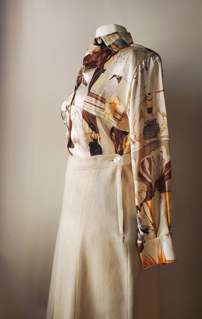 Puede incluir: Un conjunto vintage con una falda color crema y una blusa estampada. La blusa de manga larga muestra un dise&ntilde;o repetido con figuras en tonos marr&oacute;n, beige y naranja. La falda tiene cierre de bot&oacute;n y una forma sutil de l&iacute;nea A.