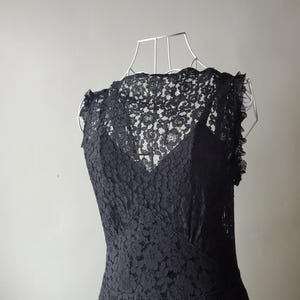 May include: A black lace dress displayed on a wire dress form. The dress features a high neckline and a fitted bodice, with a flared skirt. The intricate floral lace pattern covers the entire dress, creating a delicate and elegant look.