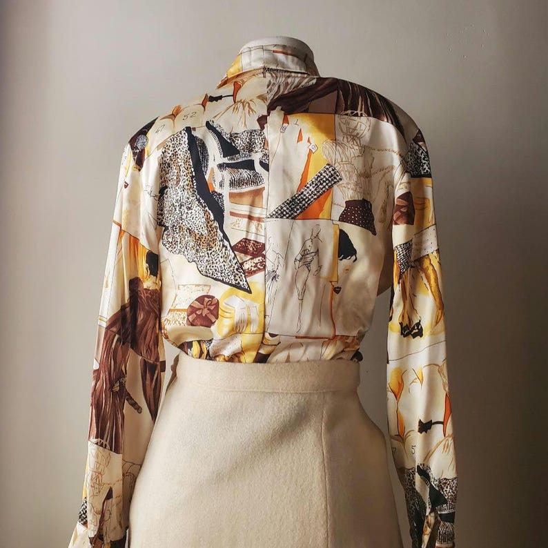 Puede incluir: Una blusa vintage de manga larga con un dise&ntilde;o de patchwork &uacute;nico. La blusa presenta un fondo color crema con varias ilustraciones abstractas y de figuras en tonos marr&oacute;n, negro, naranja y amarillo. Se combina con una falda beige.