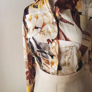 Puede incluir: Una blusa vintage con fondo crema y estampado de collage en tonos marr&oacute;n, beige y amarillo. La blusa est&aacute; abotonada y combinada con una falda crema. El conjunto se muestra en un maniqu&iacute;.