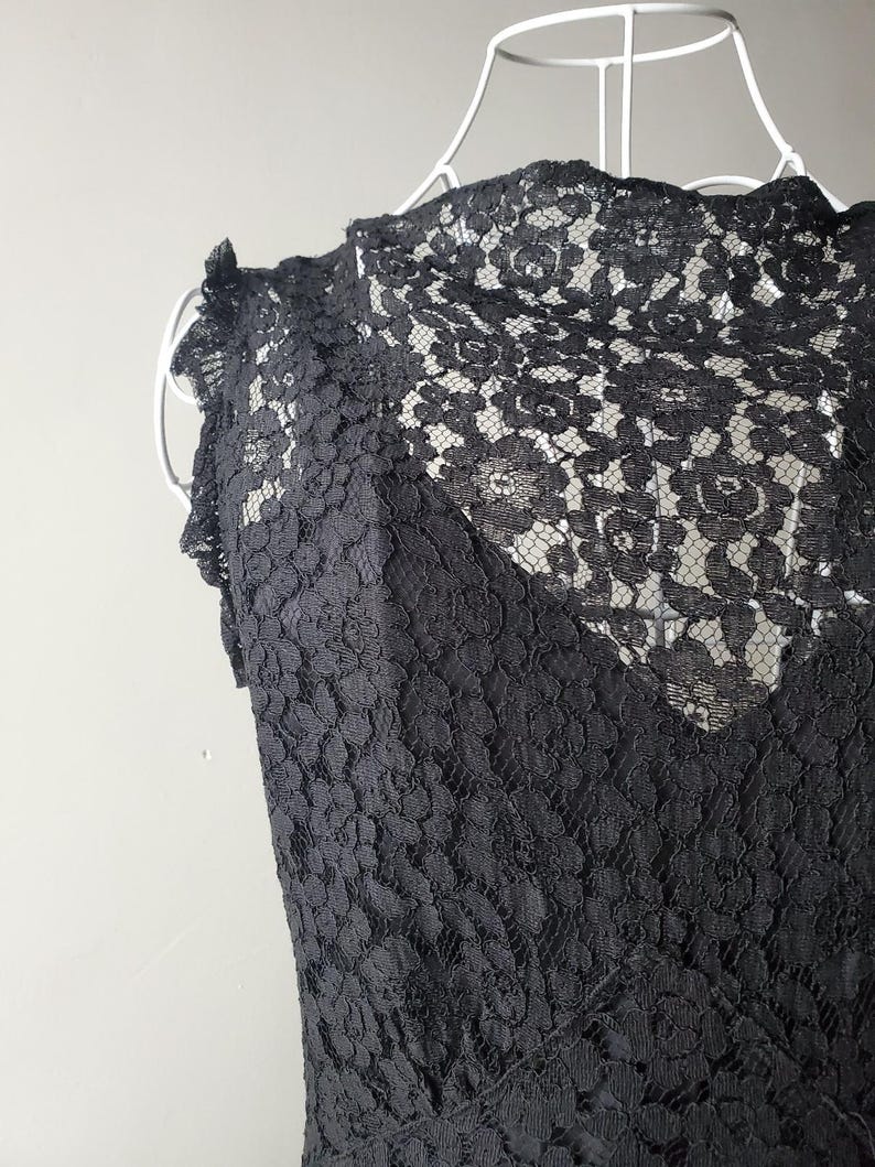 May include: A black lace top with a floral pattern. The sleeveless top features a high neckline and a delicate, textured design. The lace is intricately detailed, creating a sophisticated and elegant look.
