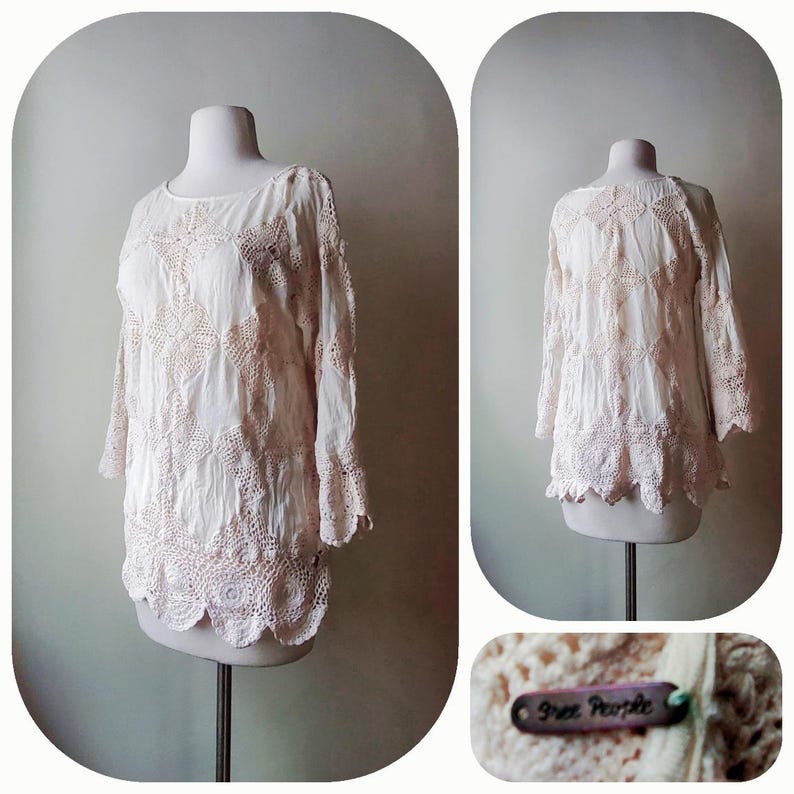 May include: Cream-colored long-sleeve top with intricate crochet detailing. The top features a round neckline, three-quarter sleeves, and a scalloped hem. The design includes floral and geometric patterns. The tag reads "Free People".