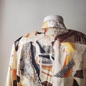 Puede incluir: Una camisa con cuello con un dise&ntilde;o de patchwork &uacute;nico. La camisa presenta una mezcla de estampados, incluyendo estampado de leopardo, formas geom&eacute;tricas y figuras abstractas en tonos crema, marr&oacute;n, negro y naranja. El n&uacute;mero "52" es visible.