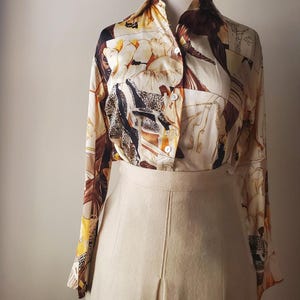 Puede incluir: Conjunto vintage de dos piezas que consta de una blusa estampada y una falda. La blusa tiene una base crema con un dise&ntilde;o marr&oacute;n y beige. La falda es de color beige claro liso. El conjunto se exhibe en un maniqu&iacute;.
