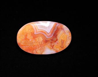 Pode incluir: Pedra de ágata oval polida, com um padrão marcante de faixas laranja, vermelhas e brancas. O design natural e rodopiante da gema é ideal para joias ou colecionismo.