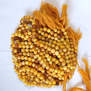 Peut inclure: Gros plan sur une collection de perles rondes jaune-brun. Les perles sont enfilées ensemble, formant plusieurs brins. L'image montre également un ensemble de pompons jaune-orange. Les perles ont un aspect marbré, avec des variations de couleur.