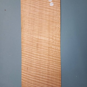 Puede incluir: Una chapa de madera con un patrón de veta distintivo. La chapa es de color marrón claro y tiene una superficie lisa. La chapa está etiquetada con el texto "GT NBS 40x58 5".