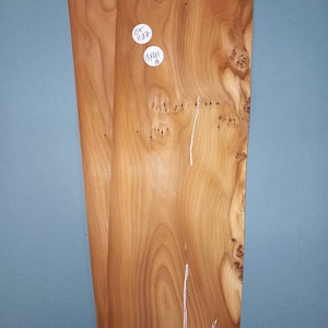 May include: Two pieces of wood veneer with a natural wood grain pattern. The wood is a light brown colour with darker brown streaks. There are two white stickers on the wood with handwritten text that reads "GT 1137" and "13X14 1/8".