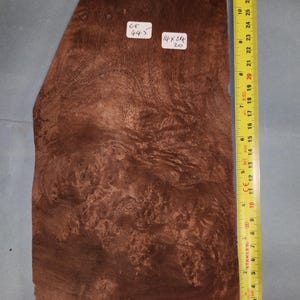 May include: A piece of wood veneer with a brown and reddish-brown color. The veneer has a unique grain pattern and is approximately 14 inches by 24 inches. The veneer is labeled "ET 445" and "14x244 20".
