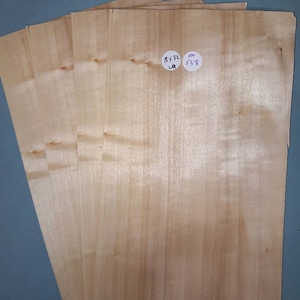 May include: Six sheets of light brown wood veneer with a subtle grain pattern. The sheets are stacked on top of each other. Two small white stickers with handwritten numbers are visible on the top sheet. The sticker on the left says "RY 32" and the sticker on the right says "6 538".