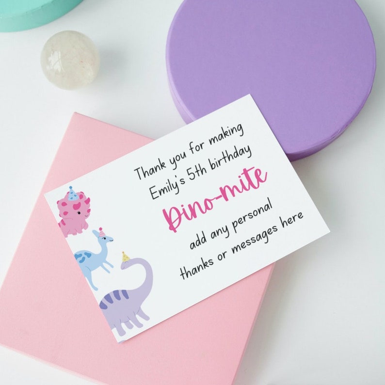 May include: A white card with the text "Thank you for making Emily's 5th birthday Dino-mite" and space for a personal message. The card features cartoon dinosaurs in pink, blue, and purple.