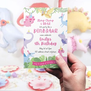 May include: A birthday invitation with a dinosaur theme. The invitation reads "Stomp Chomp & ROAR, let's party like a DINOSAUR, come celebrate Emily's 5th Birthday." The invitation is held in a hand, with dinosaur balloons in the background.