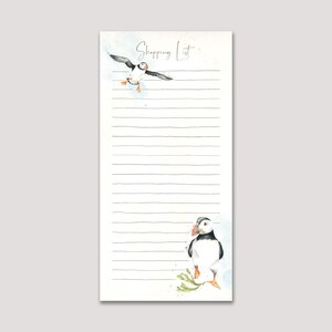 May include: A rectangular shopping list notepad with a watercolour design. The notepad features a flying puffin and a puffin standing on a rock. The words "Shopping List" are written at the top in cursive. The notepad has horizontal lines for writing.