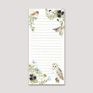 May include: A cream-coloured, lined notepad featuring a watercolour illustration of birds, butterflies, and blackberries. The birds include a sparrow, bluebird, and owl, perched on branches with green leaves. The notepad has horizontal grey lines.