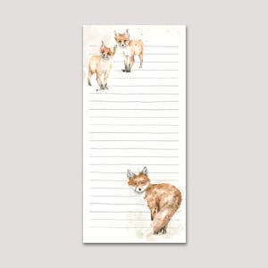 May include: A notepad with a watercolour design of foxes. The illustrations show three foxes in different poses, with orange and brown fur. The notepad has lined pages for writing and a neutral background.