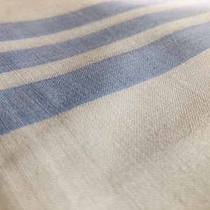 May include: Close-up of a textile featuring a repeating pattern of light blue stripes on a white background. The fabric has a textured appearance, possibly woven linen or cotton. The stripes are evenly spaced across the surface.