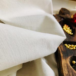 May include: A close-up of a white fabric with a smooth texture. The fabric is folded and draped over a wooden surface.