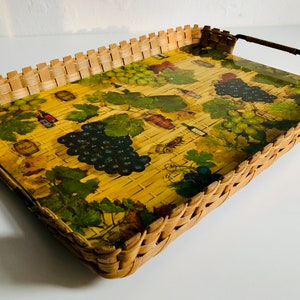 May include: A woven wicker tray with a handle. The tray has a yellow background with a printed design of grapes, vines, and wine bottles.