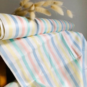May include: A roll of pastel-striped fabric in yellow, pink, blue, and green. The fabric is unrolled, showing the pattern. Dried, fluffy beige flowers are in the background.