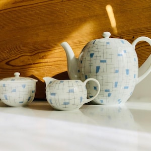 Könnte beinhalten: Ein weißes Porzellan-Teeservice mit blauem und schwarzem geometrischem Muster. Das Set beinhaltet eine Teekanne, einen Sahnekännchen und eine Zuckerdose mit Deckel. Die Teekanne hat einen gebogenen Griff und einen Ausguss.
