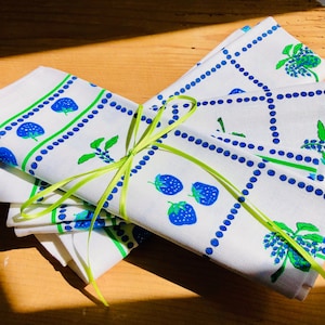 Könnte beinhalten: Ein Set aus vier weißen Baumwollservietten mit einem blauen und grünen Beerendesign. Die Servietten sind mit einem grünen Band zusammengebunden.