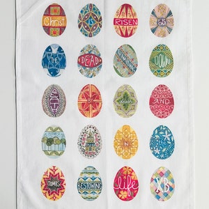 May include: A white kitchen towel featuring 16 colourful Easter eggs. Each egg has a unique design and text, including "Christ is risen from the dead" and "trampling down death and bestowing life".