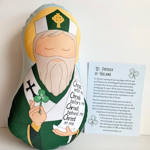 Puede incluir: Un juguete de peluche de San Patricio, una figura religiosa, con una túnica verde, barba blanca y un trébol en la mano. El juguete sostiene un rollo con el texto "Cristo conmigo, Cristo delante de mí, Cristo detrás de mí, Cristo en mí."