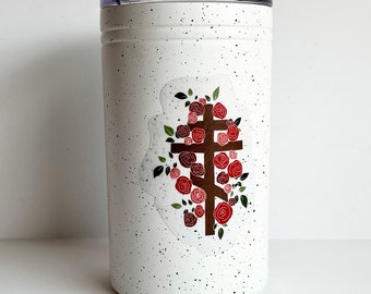 May include: White stainless steel tumbler with a speckled finish. The tumbler features a sticker of a brown cross surrounded by red roses.