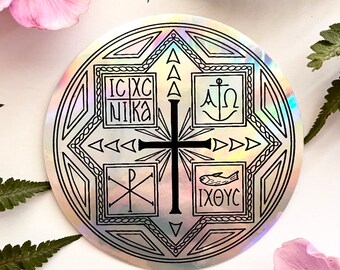 May include: A round, iridescent sticker with a black cross at the center, surrounded by geometric shapes and religious symbols. The sticker features text in multiple boxes, including "IC XC NIKA", "A Ω", "XP", and "IXΘYC".