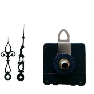 Può includere: Componenti dell'orologio su sfondo bianco. L'immagine mostra un movimento dell'orologio nero con un gancio in metallo, un quadrante nero e un dado color ottone. Sono visibili anche due lancette nere, una con un design decorativo.