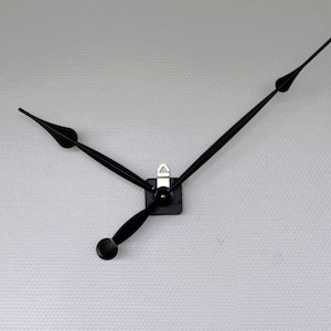 Peut inclure: Aiguilles d'horloge noires avec une pièce centrale argentée. Les aiguilles sont fixées à un fond blanc.