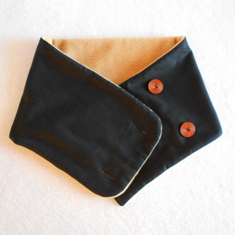 Puede incluir: Un calentador de cuello reversible negro y marr&oacute;n con dos botones marrones.