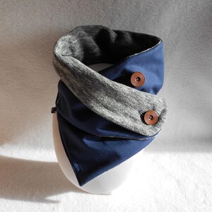 May include: A navy blue and grey reversible neck warmer with two brown buttons. The warmer is made of a soft, comfortable fabric and is ideal for keeping warm in the winter.
