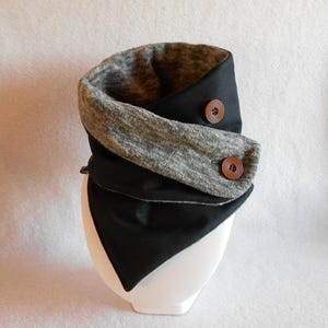 Puede incluir: Un cuello de lana negro y gris con dos botones marrones. El cuello de lana est&aacute; doblado y tiene una forma triangular.