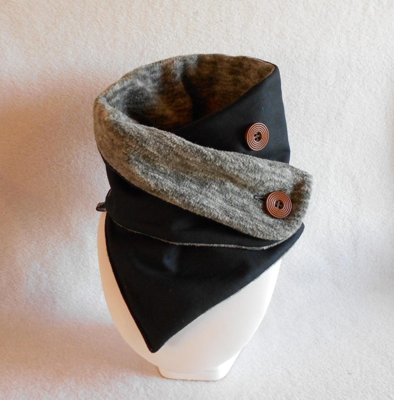 Puede incluir: Un cuello de lana negro y gris con dos botones marrones. El cuello de lana est&aacute; doblado y tiene una forma triangular.