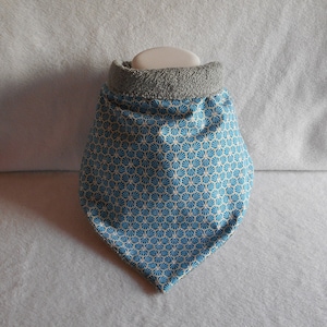 Può includere: Un bandana blu e giallo con motivo e fodera in pile grigia. Il bandana è di forma triangolare e presenta un motivo geometrico.