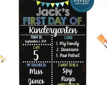 May include: A black rectangular chalkboard sign for the first day of kindergarten with colourful text reading Jack's First Day of Kindergarten, including sections for date, age, teacher, and interests, surrounded by crayons and a red apple.