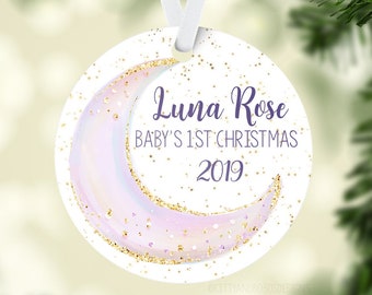 Könnte beinhalten: Runder, weißer Weihnachtsschmuck mit einem Mond-Design in Pastellviolett und goldenen Glitzerakzenten. Der Schmuck trägt den Text "Luna Rose BABY'S 1ST CHRISTMAS 2019" in lila Schrift. Ein weißes Band ist zum Aufhängen befestigt.