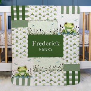 May include: A personalized baby quilt featuring a frog theme. The quilt has a green and white color scheme with a patchwork design. The name "Frederick Banks" is displayed on a green rectangle. The quilt is decorated with frog illustrations, dragonflies, and cattails.