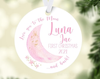 Könnte beinhalten: Ein weißer, runder Weihnachtsschmuck mit einem rosa Aquarell-Mond und goldenen Glitzerakzenten. Der Schmuck trägt den Text "Love you to the Moon, Luna Jae, First Christmas 2021...and back!" und hängt an einem weißen Band.