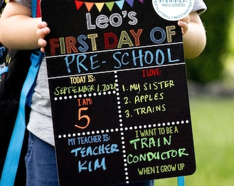 May include: A black rectangular chalkboard sign with colorful text reading Leo's First Day of Pre-School, including sections for date, age, teacher, and interests. A circular white sticker in the corner states Marker Included in blue text.
