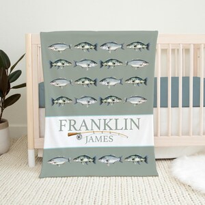 May include: A green baby blanket with a pattern of white fish and a fishing rod. The blanket has the names "FRANKLIN JAMES" printed on it.