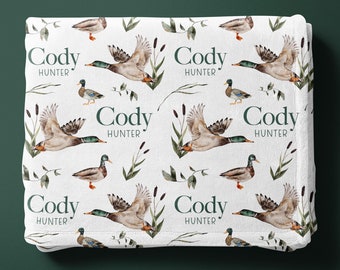 May include: White blanket with a repeating pattern of green ducks flying and the text "Cody Hunter" in green lettering.
