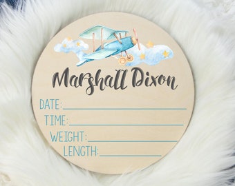 May include: A round wooden sign with a blue airplane and clouds painted on it. The sign has the text "Marshall Dixon" and spaces to fill in the date, time, weight, and length.
