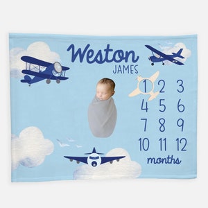 May include: A blue and white baby milestone blanket with a blue airplane, clouds, and the text "Weston James" and a number chart for each month.