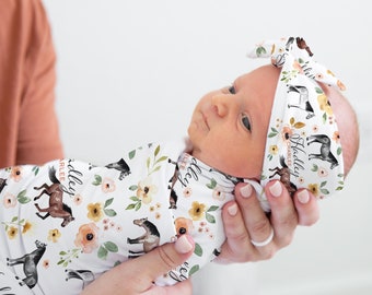 May include: A white swaddle blanket with a floral and horse print. The blanket has the text "I  Hadley  Charlie" printed on it. A baby is wearing the swaddle and a matching headband with the same print.