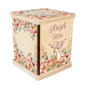 May include: Wooden piggy bank with a floral design and a fawn wearing a flower crown. The bank is personalized with the name "Hazel Rose".